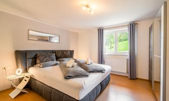 A stylish bedroom with a large bed and modern pillows. The window offers a view of a green landscape.