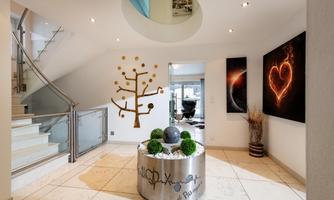 A modern entrance area with an elegant staircase and stylish wall decorations. In the center, there is a round table with plants and a decorative element.