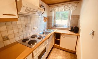A modern kitchen with a stove, a sink, and wooden shelves. The window offers a view of the outdoors and lets in plenty of light.