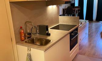 A modern kitchen unit with sink, stove, and minimalist furnishings. The floor is light and the room is well-lit.
