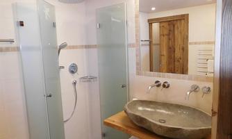 A modern bathroom with a glass shower and an elegant stone washbasin. Wood details and soft lighting create an inviting atmosphere.