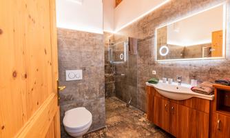 A modern bathroom with wood and stone elements. It features a shower, a sink, and a large mirror.