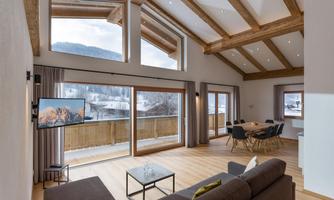 A modern living room with high ceilings and large windows. The space is bright and inviting, with a large sofa and a dining table.