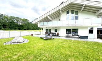 A modern house with large windows and a spacious terrace. The garden is well-maintained and offers a green lawn area.