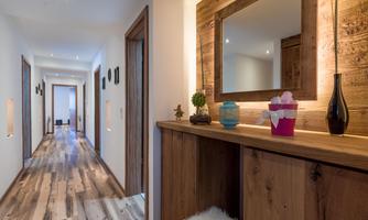 A bright hallway with wooden floors and modern walls. A dresser with a mirror and decorative plants gives the room a warm atmosphere.