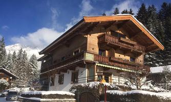 A charming chalet in winter with a snow-covered roof. Surrounded by fir trees and a clear blue sky.