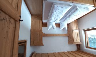 A cozy bedroom with a double bed and wooden furniture. The walls are light, and there is a window that lets in daylight.