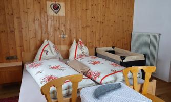 A cozy bedroom with wooden paneling. It contains two beds, a crib, and a table.