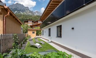 A modern building with a beautiful terrace and loungers in the garden. In the background, mountains and traditional huts can be seen.