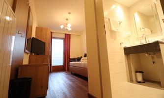 A modern room with wooden flooring, a TV, and a large window. The bathroom is bright and well-equipped.