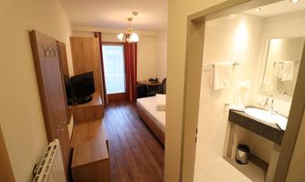 A cozy hotel room with a double bed, a television, and a modern bathroom. Bright walls and wooden flooring create an inviting atmosphere.