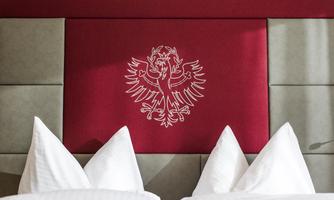 An elegant headboard in red with an embroidered coat of arms. In the foreground, padded pillows are visible.