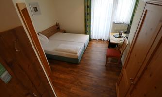 A simple bedroom with a bed and a desk. The room has large windows that let in daylight.
