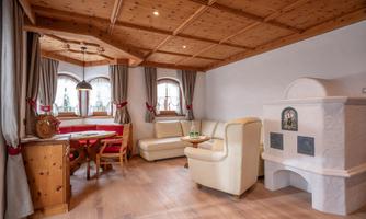 A cozy living room with wooden ceilings and large windows. There is a bright sofa area and a wooden dining space.