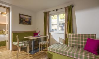 A cozy living room with a wooden floor. There is a seating area with a colorful sofa and a dining area.