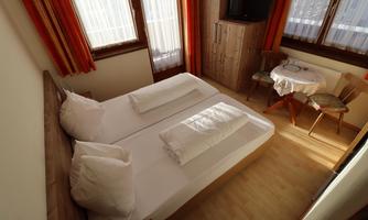 A cozy bedroom with two single beds and plenty of natural light. There is a small table and chairs in the corner.