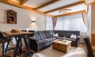 A cozy living room with a large sofa and a wooden table. Bright walls and natural wood elements create a welcoming atmosphere.