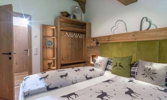 A cozy bedroom with a double bed and modern wooden furniture. The walls are green, and the bedding is decorated with reindeer.
