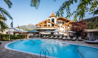 A stylish hotel with an inviting pool and sunbeds. In the background, there are mountains and a clear sky.