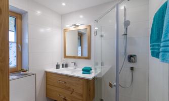 A modern bathroom with a shower and a wooden washbasin. There is a large mirror and towels in turquoise.
