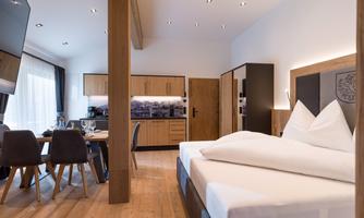 A modern room with a large bed and an adjoining kitchenette. The cozy atmosphere is emphasized by wooden details and warm colors.
