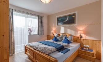 A cozy bedroom with a large bed and wooden furniture. The room has daylight through a window and soft lighting.