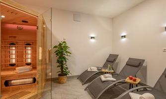 A relaxing wellness room with loungers and a sauna in the background. The room is modernly furnished and has a pleasant atmosphere.