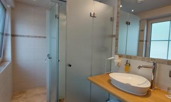 A modern bathroom with a glass shower cabin and a stylish sink. Bright tiles and a wooden shelf create an inviting atmosphere.