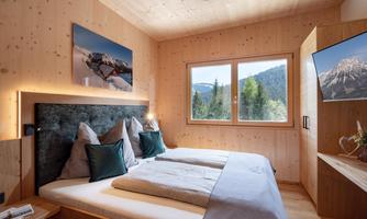 A modern bedroom with wooden decor and a large window overlooking a green landscape. The beds are comfortable and inviting with pillows and blankets.