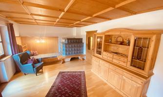 A cozy room with wooden ceilings and a carpet. On the left side, there is a blue armchair, and on the right side, there is a wooden sideboard.