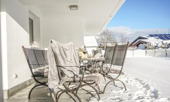 A winter balcony with white snow covers. Chairs with a blanket and a bright blue sky in the background.