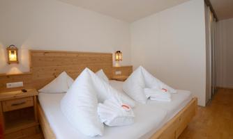 A cozy bedroom with a wooden bed and large pillows. The warm walls and lighting create an inviting atmosphere.