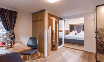 A modern room with wooden flooring and stylish furnishings. The room features a table, chairs, and an adjacent sleeping area.
