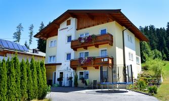 A beautiful, bright building with wooden cladding and balconies. In front of the house, there is a well-maintained garden and an inviting driveway.