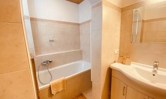 A modern bathroom with a bathtub and a sink. The walls are tiled in light colors, and there is a mirror above the sink.