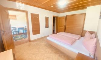 A bright bedroom with two beds and pink bedding. In the background, chairs and a table are visible.