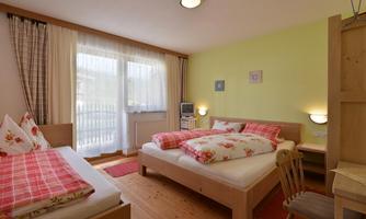 A cozy bedroom with two beds and a bright, friendly wall color. Large windows provide plenty of daylight and a pleasant atmosphere.