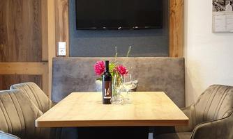 A cozy dining room with a wooden table and modern chairs. In the background, there is a television and fresh flowers on the table.