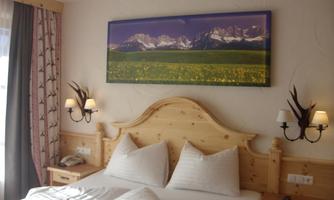 A cozy bedroom with wooden beds and beautiful pillows. A picture of a landscape and mountains is hanging on the wall.