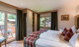 A cozy bedroom with a large bed and a balcony. The room has bright colors and windows that let in plenty of daylight.