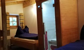 A cozy sleeping room with two single beds and a modern bathroom. The walls are made of wood, and large windows let in natural light.