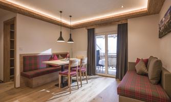 A cozy living space with a dining table and a bench in modern Alpine style. Large windows provide access to the balcony and lots of daylight.