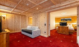 A cozy hotel room with wooden paneling and a red carpet. There is a sofa as well as amenities such as a television and a view of the bedroom.