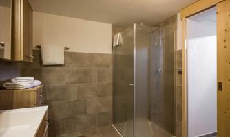 A modern bathroom with a glass shower and wooden details. There is also a sink and some towels.