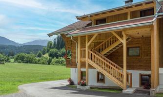 A charming wooden house with a staircase and blooming plants. In the background, green meadows and gentle hills can be seen.