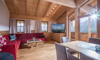 A cozy living room with wood paneling, a red couch, and a large window with a mountain view. The table is set for four people.