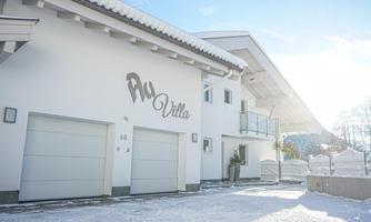 A modern, snow-covered house with the inscription "Aqua Villa". The facade is bright and inviting under a clear sky.