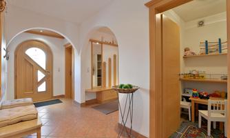 A bright hallway with wooden and tiled flooring. On the right side, there is a small room with toys and a table for children.