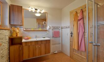 A modern bathroom with wooden cabinets and a large mirror light. There is a shower, towels in various colors, and a warm atmosphere.