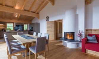 A modern living and dining room with a wood ceiling. A large table and a cozy fireplace create an inviting atmosphere.